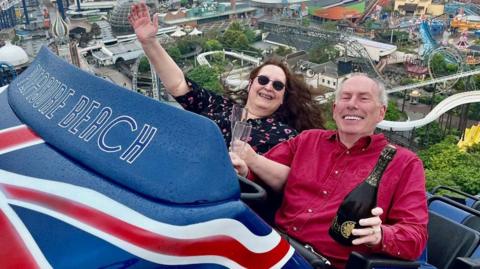 Mark Cook and Carole Noel on rollercoaster at Blackpool Pleasure Beach with champagne 