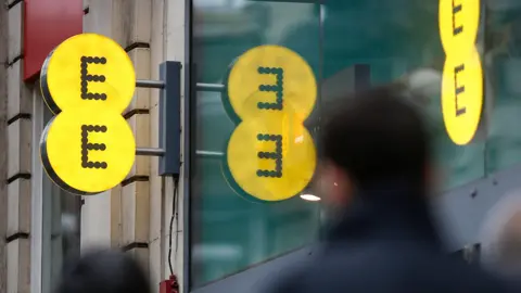 Getty Images A yellow EE sign outside a high street shop. The logo is reflected in the shop window.