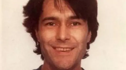 Grainy textured older photo of Scozzi smiling at the camera. He has dark hair and brown eyes