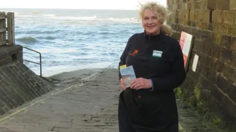 Coast to Coast Passport A woman stands by the sea and holds up a passport.
