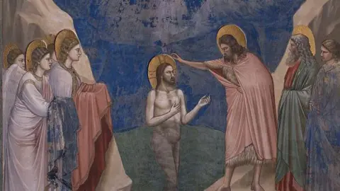 Getty Images A close-up of the Baptism of Christ (Battesimo di Cristo), by Giotto, 1303-1305, 14th Century, fresco Italy, Veneto, Padua, Scrovegni Chapel. It is a colourful scene showing Jesus Christ is naked and waist-deep into the water of the Jordan River, flowing between two mountains; He raises his arms towards St. John the Baptist, who blesses him from the right bank; on the right bank an old man with halo and long beard and a young man are waiting to be baptised, while on the left four angels stand, holding out to Christ the garments he was previously wearing. 