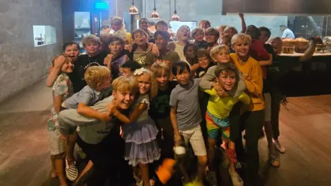 Contributed A group of about 30 children pose for a photo within a hotel dining room. They are smiling and many are hugging each other.