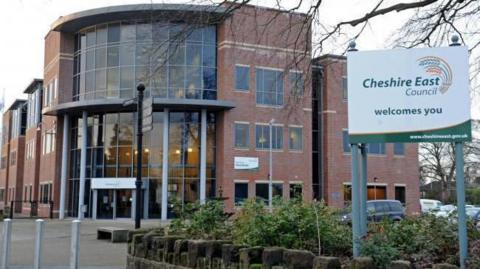 The entrance to the Cheshire East headquarters, with a white, green and orange sign outside saying 'Cheshire East welcomes you'