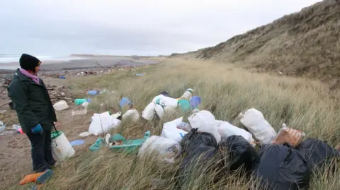 BEACH BUDDIES A woman wears a hat and looks out at all the rubbish strewn across Ballaugh Beach.