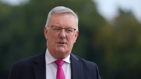 PA Media Health Minister Mike Nesbitt in a navy suit jacket white shirt and pink tie