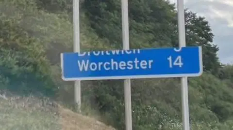 A partially complete blue motorway sign. The sign reads "Worchester" and states that the city is 14 miles away.