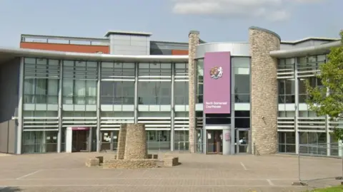 A large municipal building with a purple facade reading "North Somerset Court House". A large brick concourse sits in front of the building.