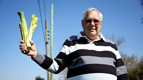 Barry Goodwin / Cover Photos A man holding a stick of celery stood in front of a telephone pole.