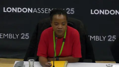 London Assembly A woman in a red top sits at a desk in a green lanyard at the London Assembly.