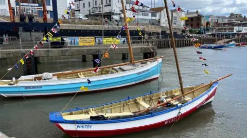 Two fishing cobles in Bridlington Harbour. The one nearer the camera has "WHITBY" painted on it. It is red, white and blue. The one further from the camera has "BRIDLINGTON" and "THREE BROTHERS" painted on it. It is light blue and white.