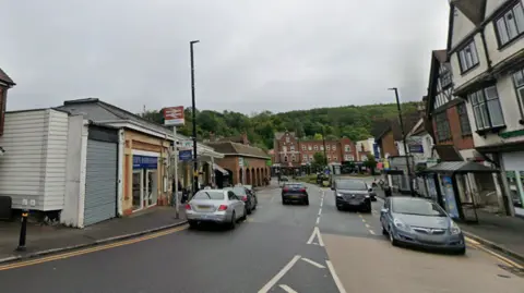 A view of the road. There is a railway station and several cars driving past.