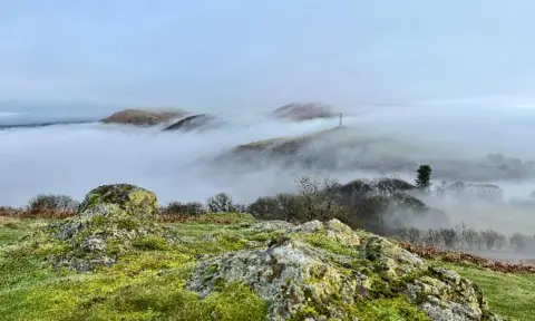 BBC Weather Watchers/Snapper Simon Cloud and mist can be seen blanketing hills in Church Stretton. Several hills are seen emerging from mist and fogs with some trees.