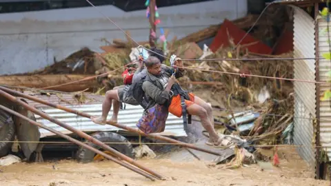 Getty Images Two men hang from  zipline over floodwater