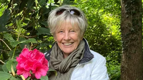 Jeanette has short blonde hair and is wearing makeup and a white coat.