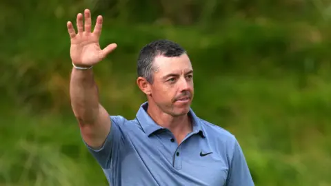 PA Media Rory McLeill, vestindo uma camisa de golfe azul clara com cabelos pretos curtos. Ela está segurando as mãos no ar. 