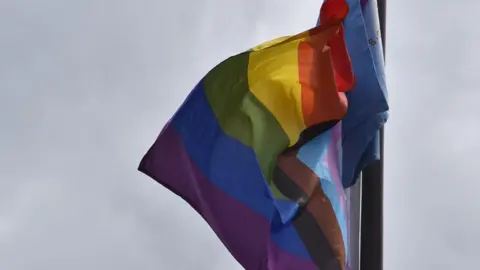 Beth Underwood A rainbow flag blows in the wind against the sky.