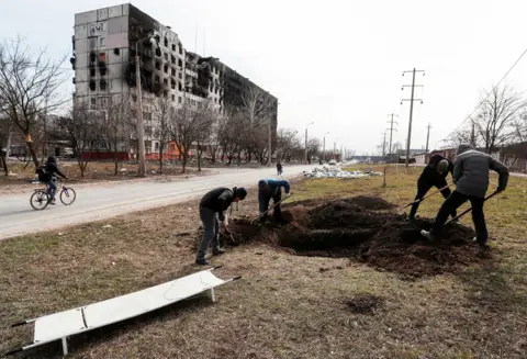 Reuters Digging graves by the roadside in Mariupol, 20 March