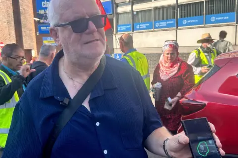 PA Media A man with short white hair, holding up his phone, showing a picture of a thermometre 