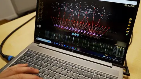 Laura Foster/BBC A hand on a laptop displaying a computer simulation of fireworks.