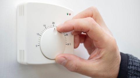 A wall mounted thermostat being adjusted by hand