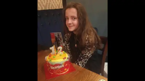 Family handout Charley Patterson is sitting with a cake on her 12th birthday. The cake is a 'Skittles' cake. She has brown hair and is wearing a dress with leopard spotted sleeves.