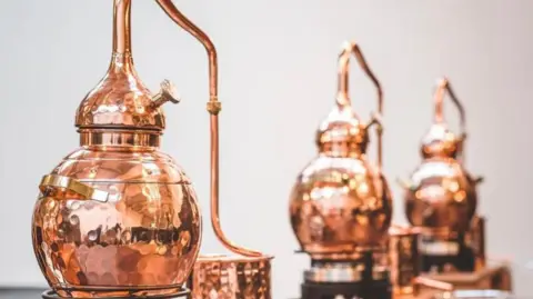 Exeter Gin A row of small copper stills with the first still more in focus and the second and third increasingly blurred