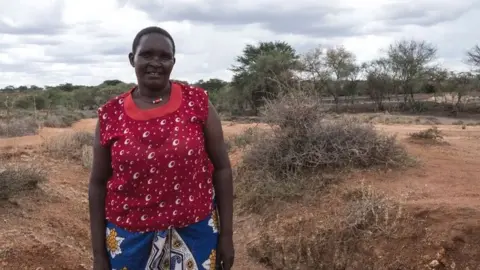 A Kenyan woman standing in a barren landscape with sparse trees