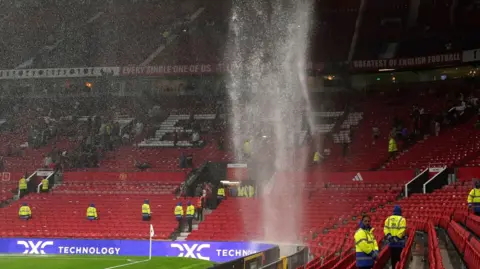 Heavy rainfall pours from the stand roof on to empty seats at Old Trafford