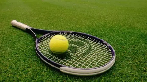 BBC tennis ball on top of a racquet on grass