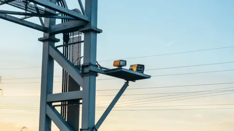 Getty Images A stock image showing a traffic camera fixed to a metal motorway gantry. It appears to be dusk and the blue sky is turning soft and yellow.