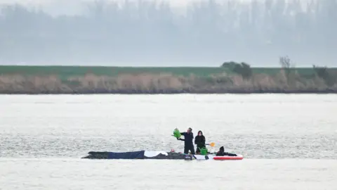 People next to a humpback whale stranded on a sandbank,