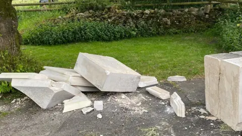 A stone pillar that has collapsed onto tarmac. 