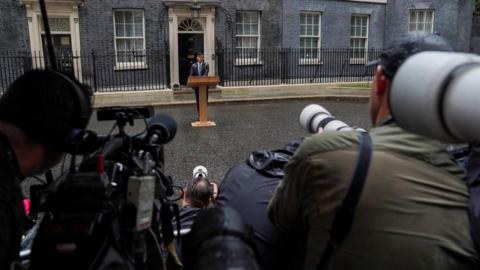 Cameras in the foreground, Rishi Sunak standing by a lectern in Downing Street in the background