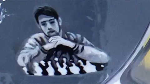 Getty Images Close up of the helmet featuring an image of Oleksiy Lohinov, who is resting his hands on his chin and has dark hair and a beard.