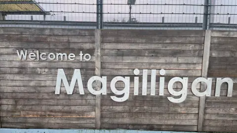 'Welcome to Magilligan' sign on wood fencing.