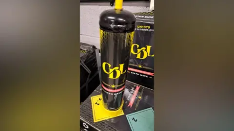 Durham Police A tall canister with a black and yellow design. A yellow logo on the front reads: "CDL." And text underneath reads: "Sixth wave." The canister is placed on top of a black and yellow box. It has a yellow spout.