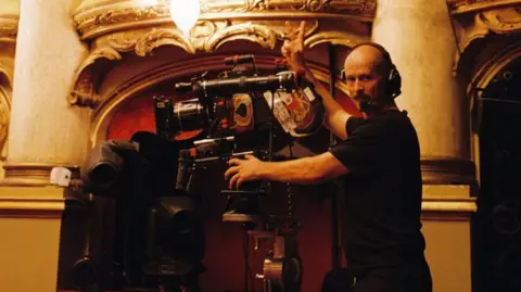 Mats Hoiby Lars Thomas Skare, on a film set behind a camera, wearing a headset, with two fingers raised