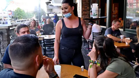Reuters Waitress serves customers while masked