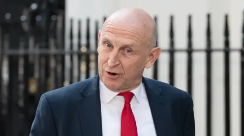The UK's new chancellor John Healey wears a dark blue suit jacket, a white shirt and a red tie 