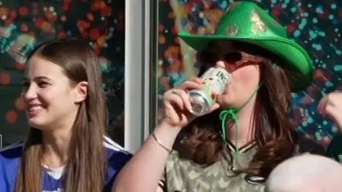 A girl with a green cowboy hate swigs a can of drink