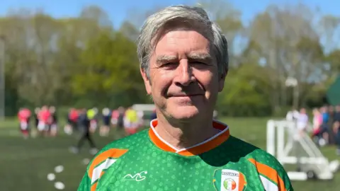 Michael O'Byrne stood in a green orange and white ireland t-shirt on a astro turf pitch smiling at the camera.