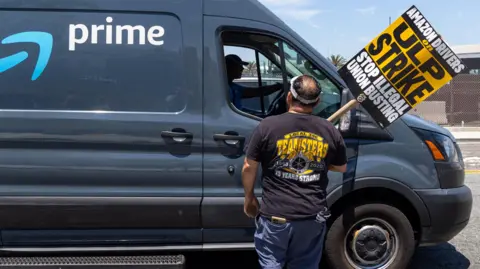 Getty Images Teamsters union members talks to a truck driver at an Amazon facility in Los Angeles during a labour a strike in 4 August, 2024.