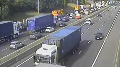 A CCTV image of queuing traffic on a motorway carriage. Several lorries can be seen in the first and second lane.