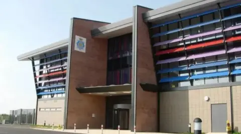 Cumbria Constabulary's headquarters. It has a police badge on the side of the building and multi-coloured panelling. It is a modern building 