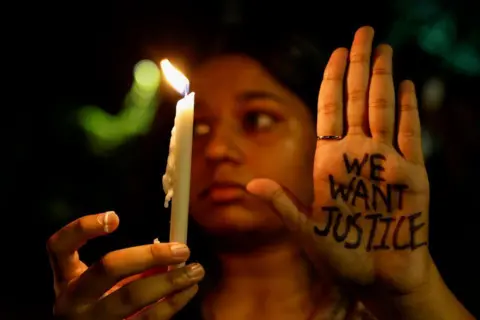 Reuters A woman holds a candle during a vigil to condemn the rape and murder of a medical student at a government hospital in Kolkata, on a street in Mumbai, India, August 14, 2024