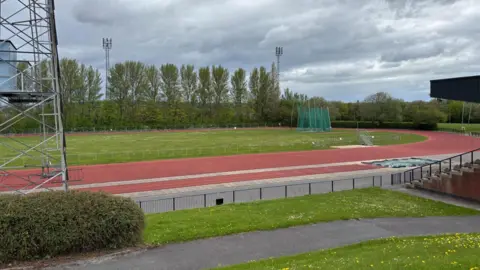 Simon Thake/BBC An outdoor athletics track surrounded by grass verges and a small spectator seating area