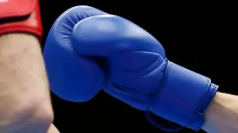 Reuters Close up of a blue boxing glove held up towards a red boxing glove in a boxing ring