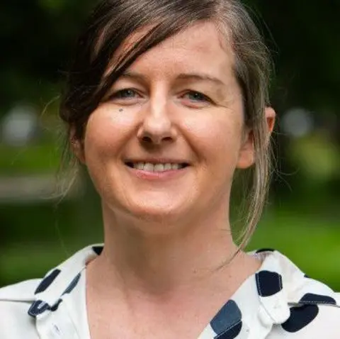 Scottish Green Party A woman with tied-up brown hair, wearing a white and black top, smiles at the camera.