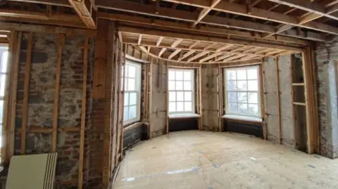 Supplied/National Capital Commission An image showing the inside of the residence with its walls and floors stripped, showing the wooden foundation of the structure. The image in particular shows a rotunda inside the house with three large white windows overlooking the exterior.