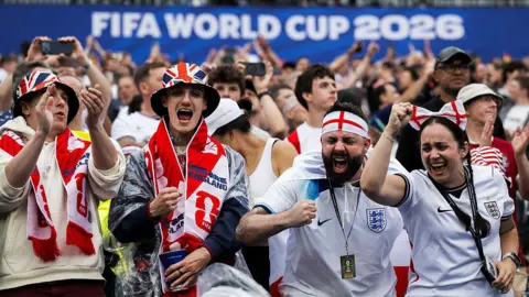 Getty Images Fans inside a football stadium draped in red and white scarves and wearing white football shirts. 